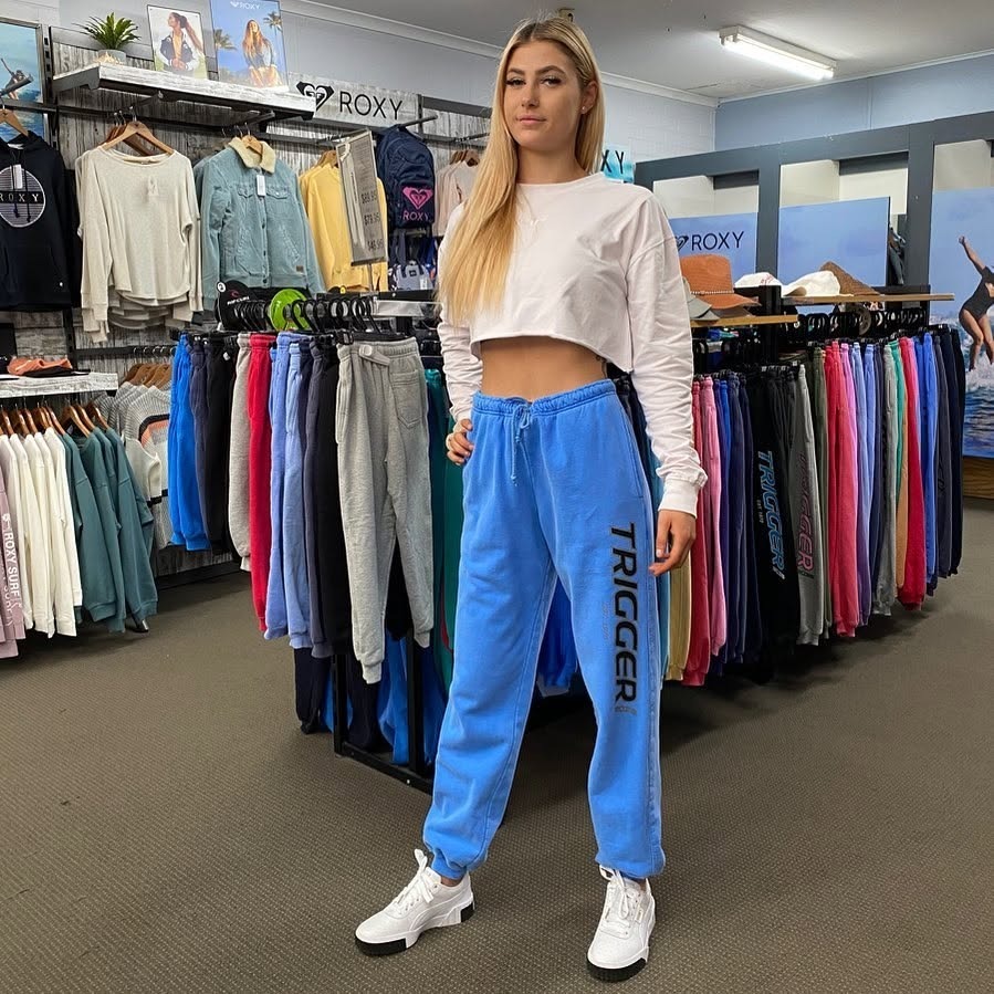 Trigger Bros Tracksuit pants Model wears a pair of Cobalt Blue Trigger Bros tracksuit pants in front of a rack of coloured track pants